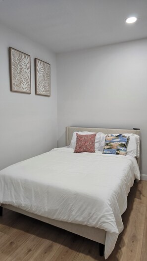 Une chambre à coucher avec un lit, du linge de lit blanc, deux œuvres d’art accrochées au mur et un luminaire au plafond.