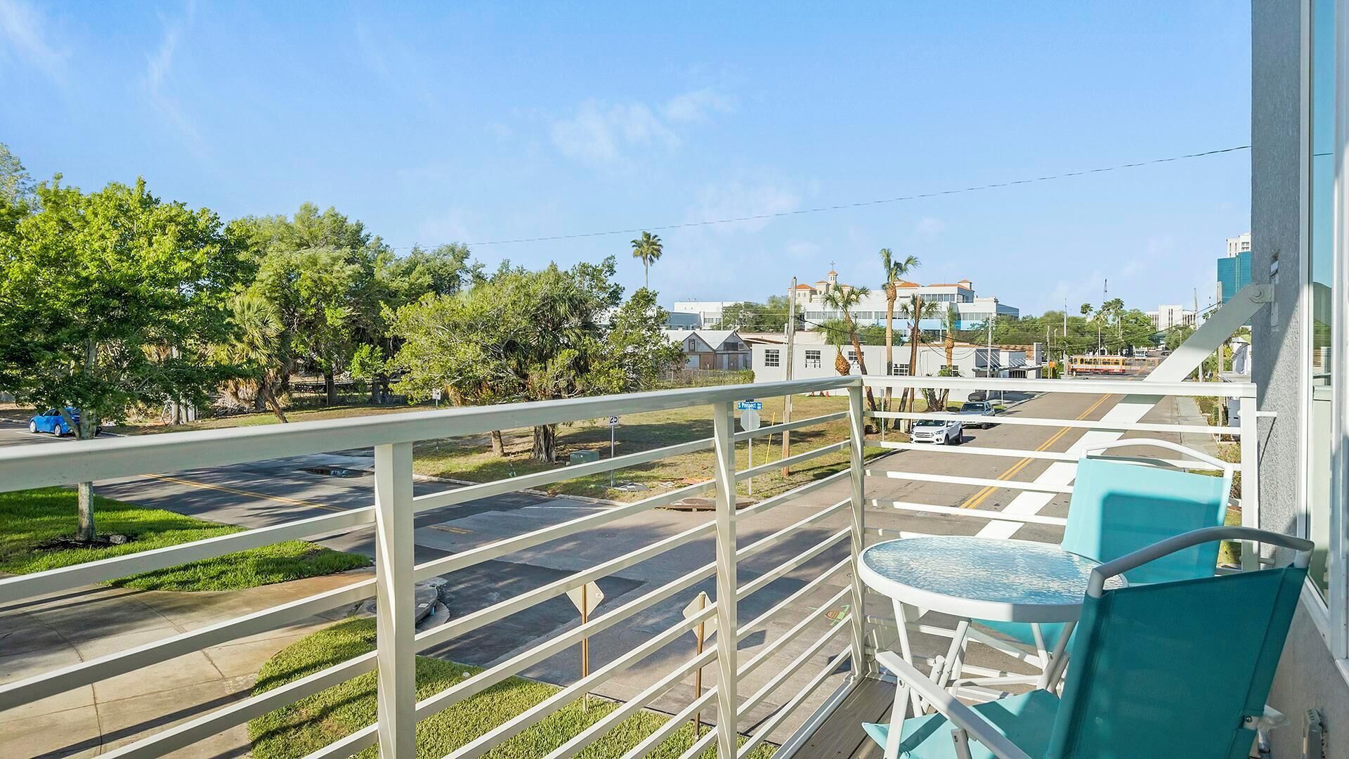 A balcony with a view of a street, a parking lot, and buildings in the distance.