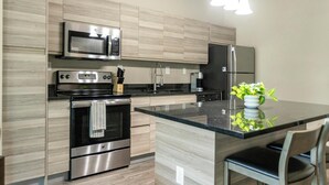 A modern kitchen with stainless steel appliances, a central island, and light wood cabinetry. - Landing | Chic 1BD, Gym, Yoga Studio (Clearwater)