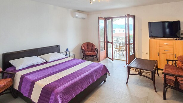 Ett hotellrum med en säng, ett skrivbord, en stol, en tv och en balkong.