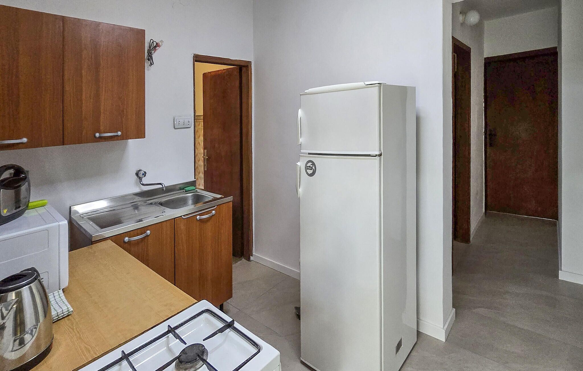 A compact kitchen with a gas stove, a sink, a white refrigerator, wooden cabinets, and a door leading to another room.
