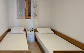 Ein kleines, sauberes Zimmer mit zwei Einzelbetten, einem hölzernen Kopfteil, einem kleinen Nachttisch und einem Fenster mit Ausblick.