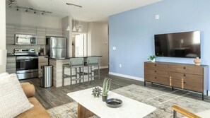 Eine moderne Küche mit Edelstahlgeräten, eine Essecke mit Barhocker, ein Flachbildfernseher und ein Holzschrank.