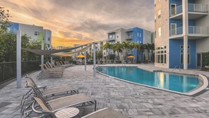 A pool area with lounge chairs and umbrellas, surrounded by multi-story buildings with balconies. - Landing | Stunning 1BD, Pool, Gym (Clearwater)