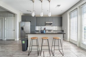 Eine moderne Küche mit grauen Schränken, einem Edelstahlkühlschrank, einer Mikrowelle, einem Spülbecken und einer Bar mit Hockern.