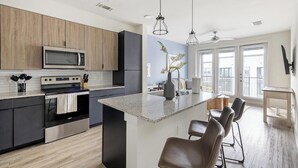 A modern kitchen with a central island, bar stools, and a dining area. - Landing | Incredible 1BD, Clubhouse, Gym (Lewisville)