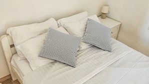 Een bed met witte beddengoed, twee gestreepte kussens en een bedlamp op een nachtkastje.