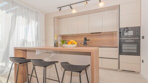 A modern kitchen with a wooden island, bar stools, a built-in oven, and a large window with sheer curtains. - Nice home in Bristani with sauna (Bristani)