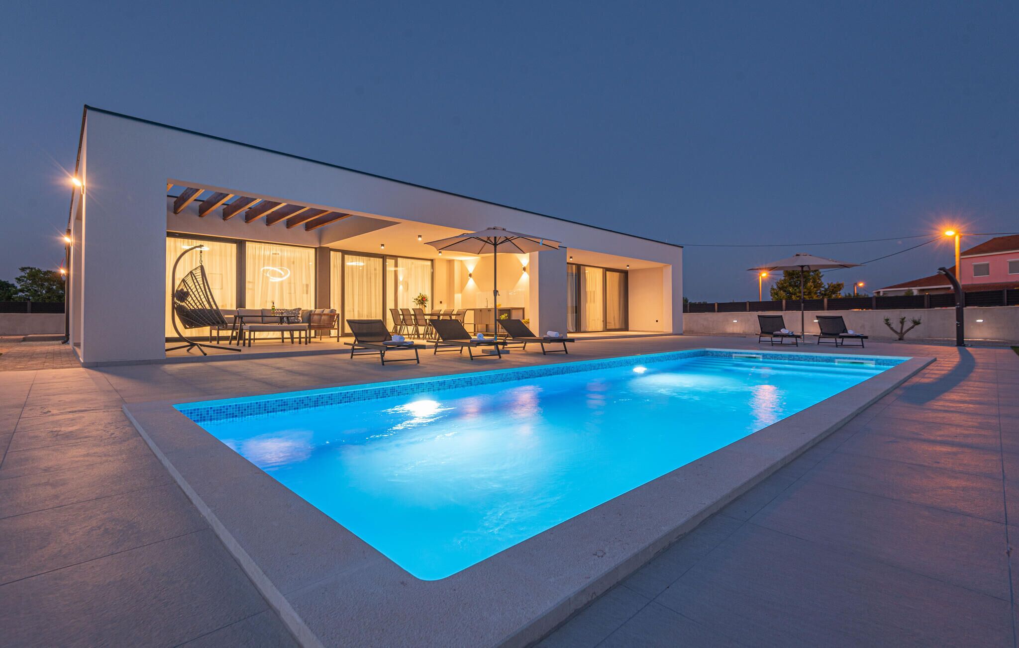 Ett modernt hus med en swimmingpool, utomhusmöbler och en väl upplyst uteplats.