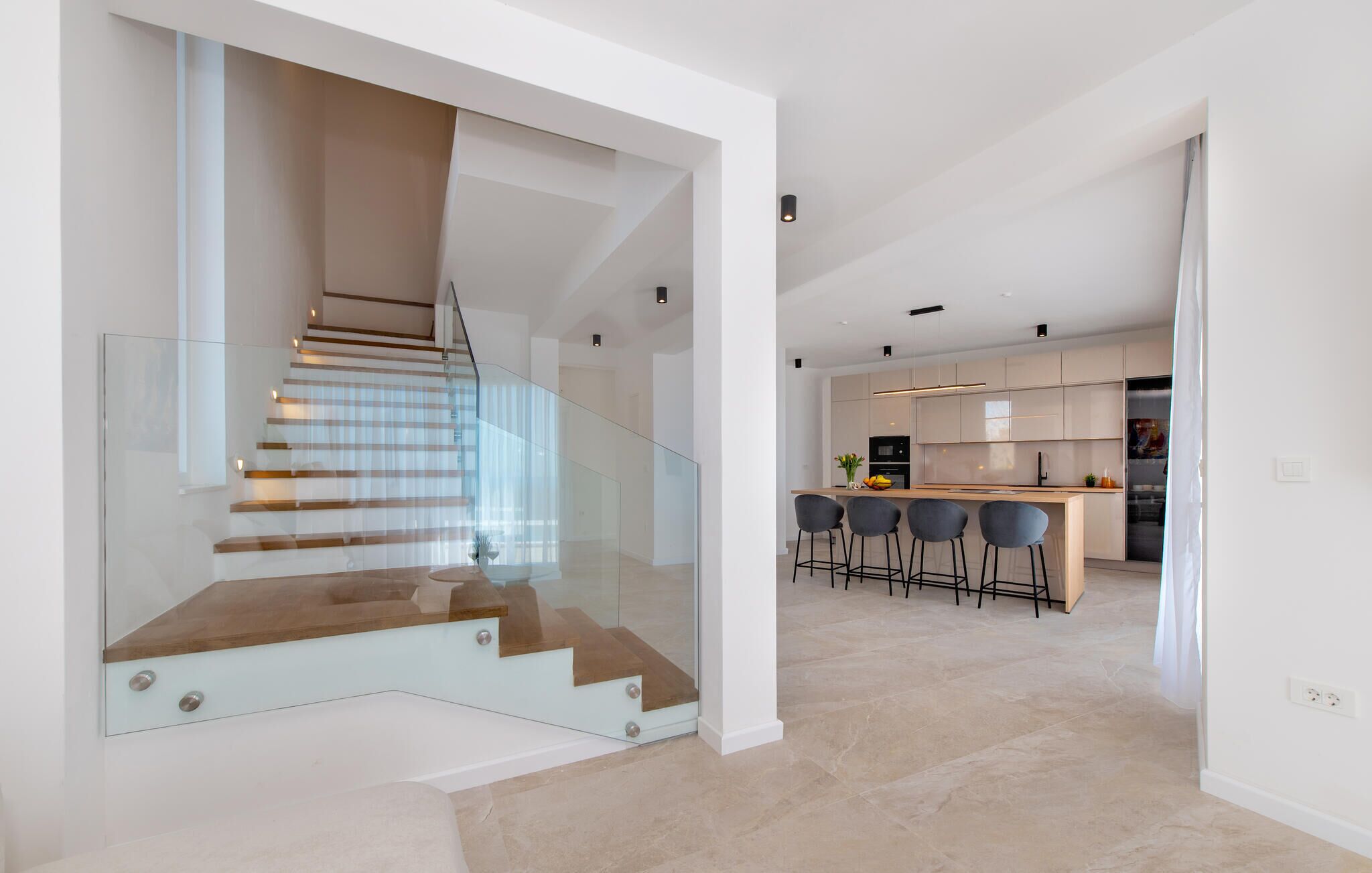 Un interior moderno con una escalera de cristal, una cocina con taburetes de bar y un diseño minimalista.