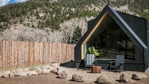 A modern cabin with a triangular roof, large windows, and a seating area with chairs.
