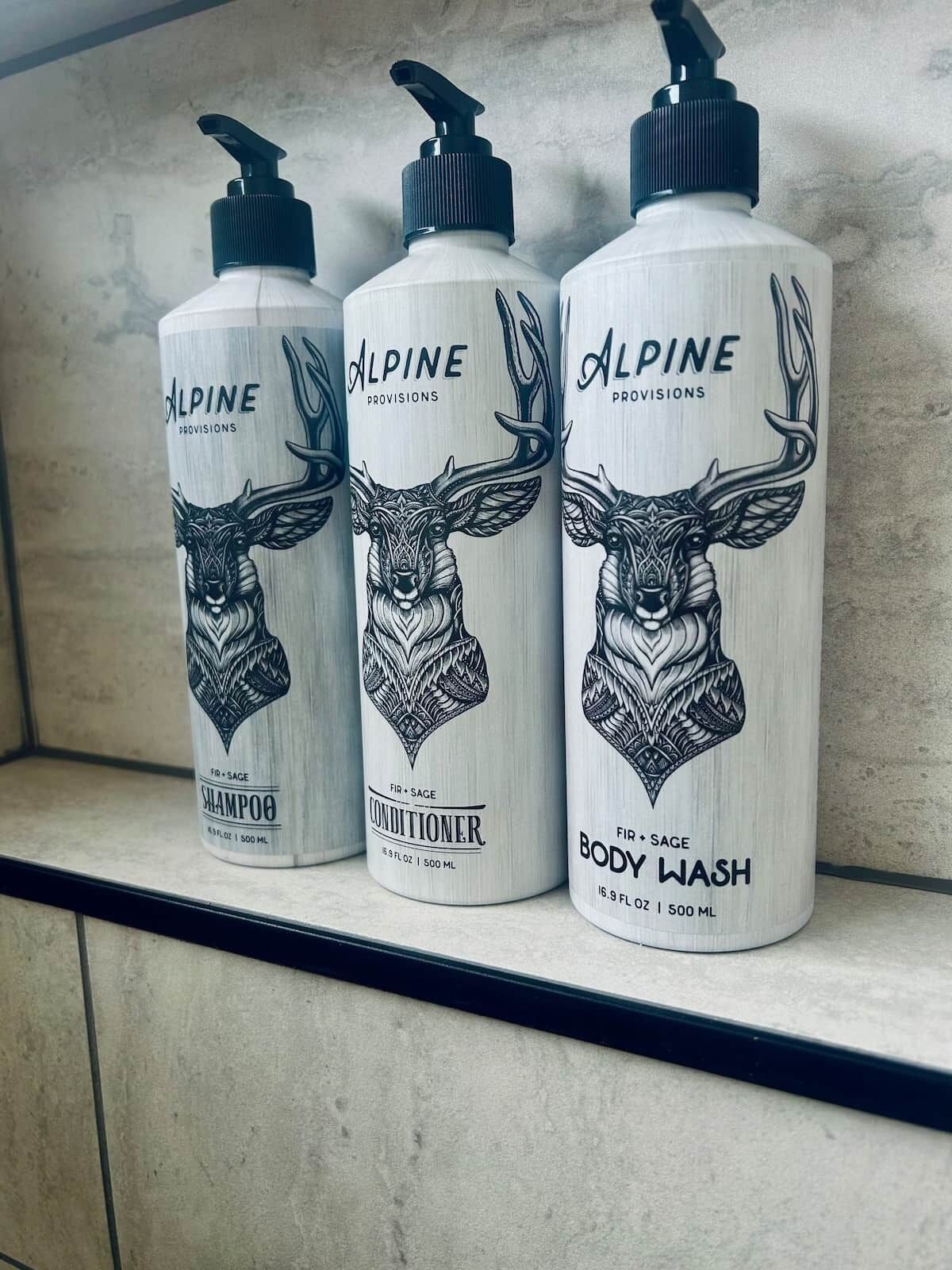 Drie flessen Alpine Provisions producten: shampoo, conditioner en douchegel, elk met een illustratie van een herten en een pompdispenser.