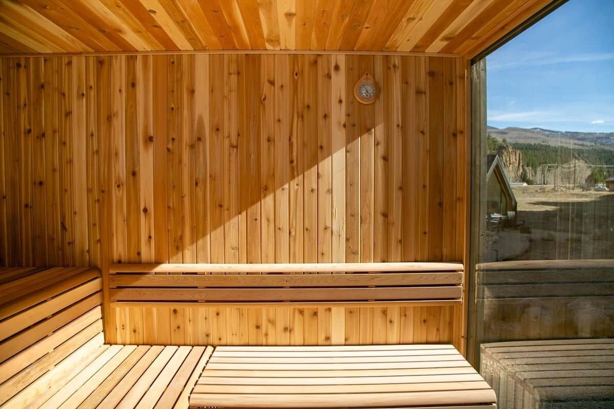 Ein Saunaraum mit Holzwänden und -bänken, einer Uhr sowie Blick ins Freie.