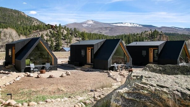 Three modern cabins with large windows, set in a mountainous area with a clear sky.