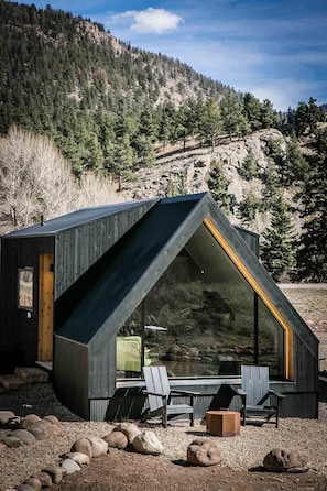 A modern cabin with a sloped roof, large windows, and a seating area with chairs and a table.