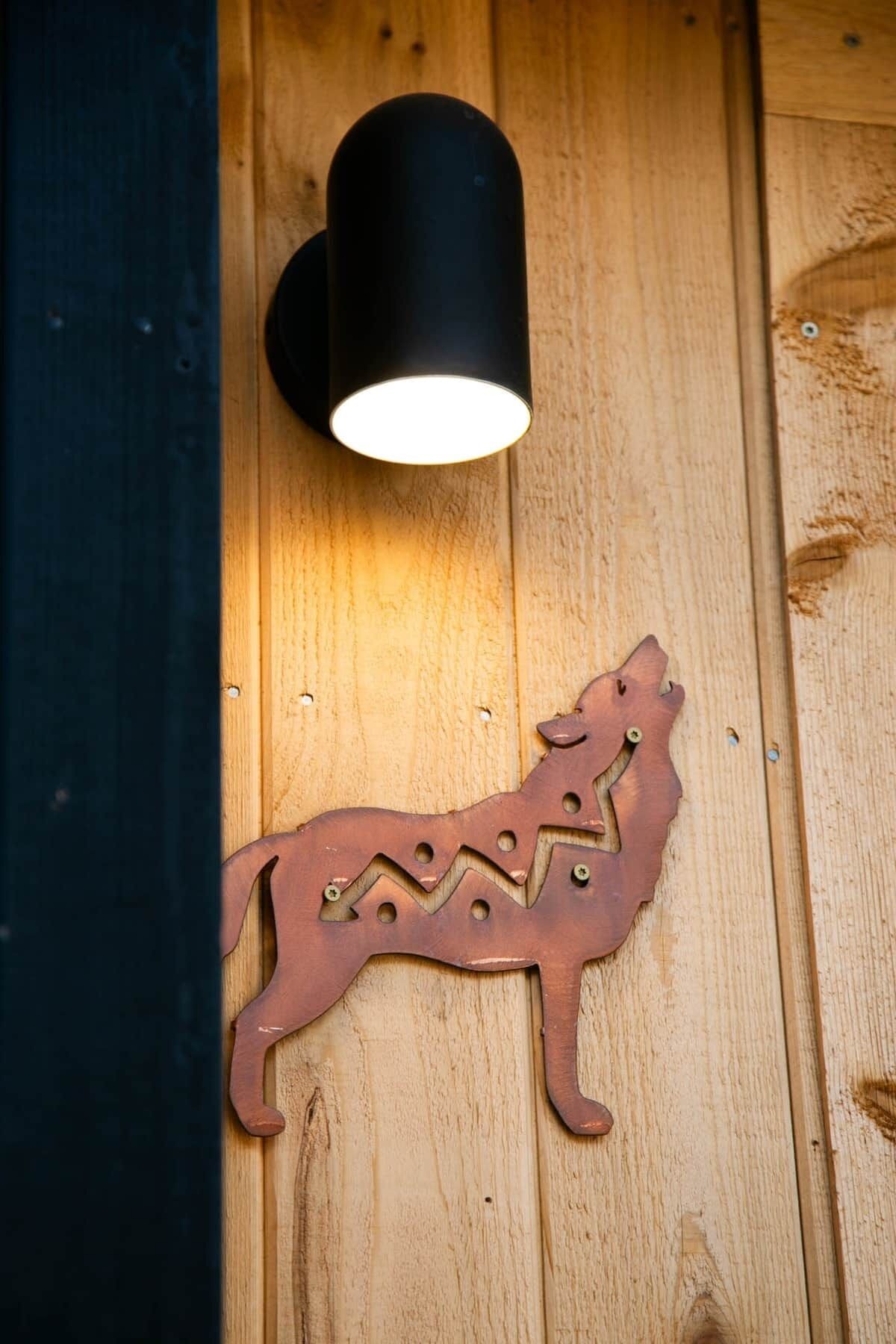 A wall-mounted light fixture and a wooden wolf silhouette decoration on a wooden surface.