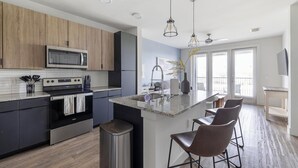Een moderne keuken met een centraal eiland, barkrukken, een magnetron, oven en een spoelbak.