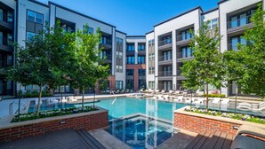 A modern apartment building with a central swimming pool, surrounded by lounge chairs and trees. - Landing | Stylish 1BD, Courtyard, Gym (Lewisville)
