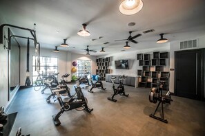 A gym with stationary bikes, ceiling fans, and a TV on the wall. - Landing | Stunning 2BD, Gym, Clubhouse (Lewisville)