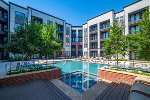 A modern apartment building with a central swimming pool, surrounded by lounge chairs and trees. - Landing | Incredible 2BD, Clubhouse, Gym (Lewisville)