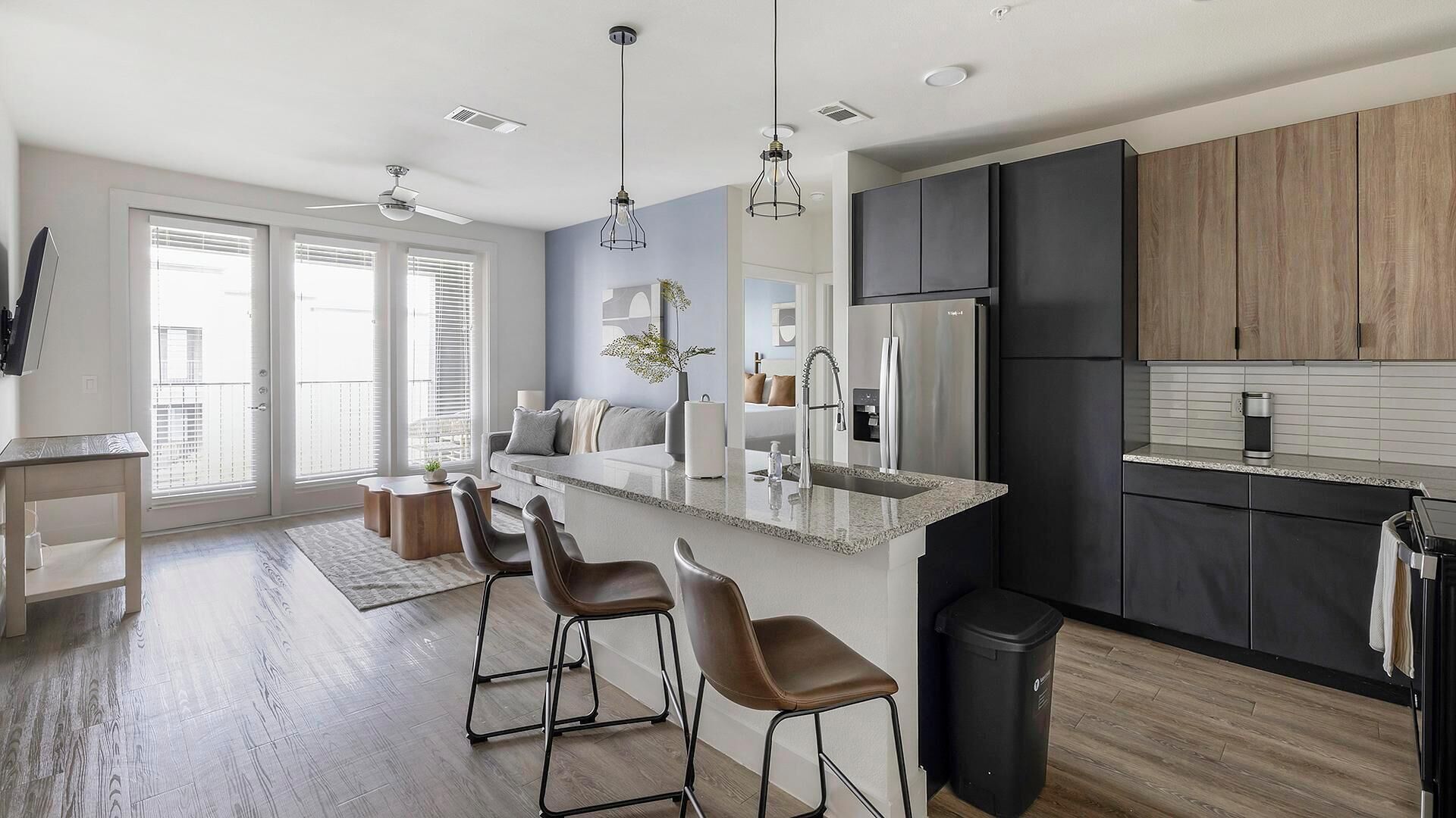 A modern kitchen with a central island, bar stools, a refrigerator, and a trash can.