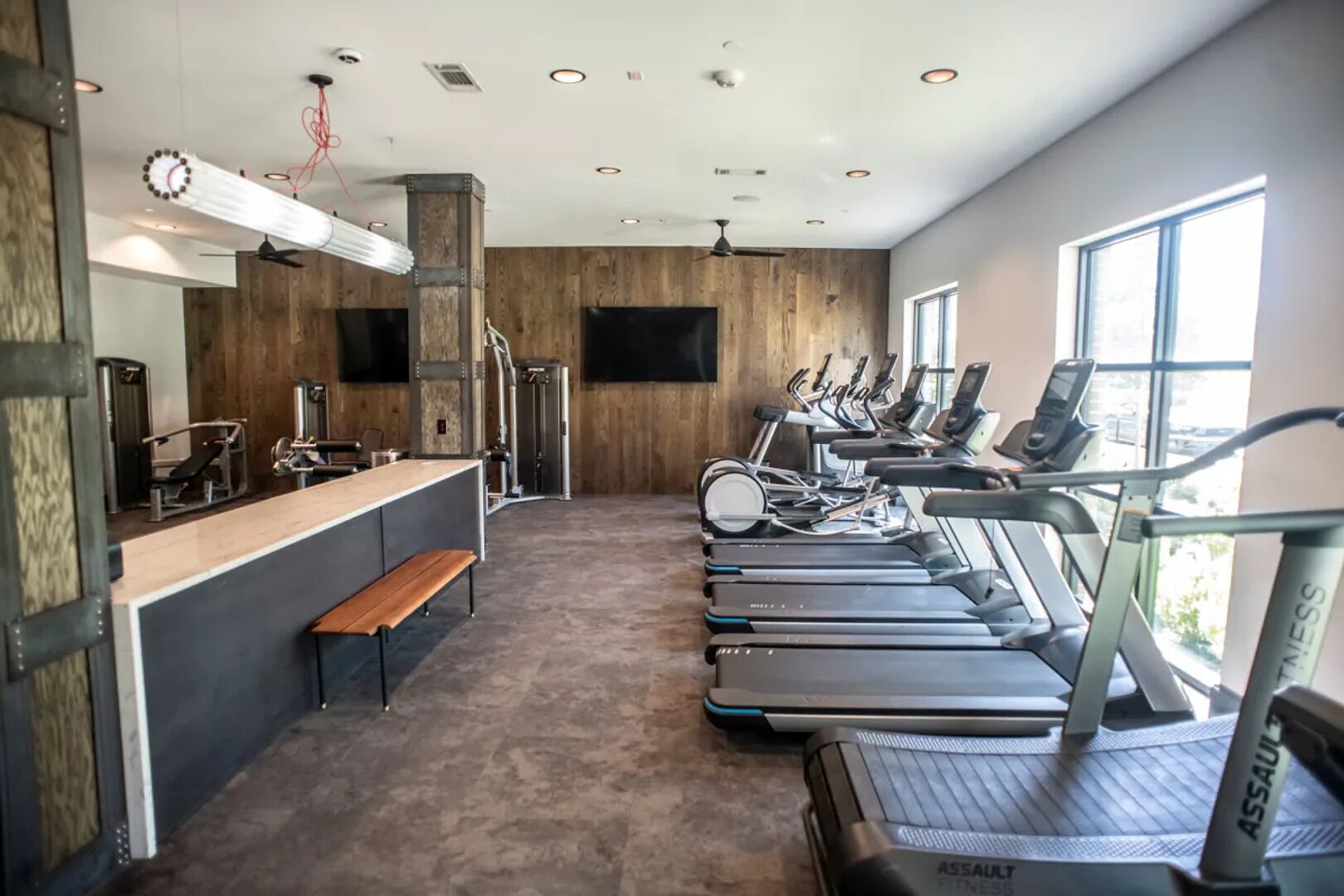 A gym with treadmills, a bench, a weight machine, and a TV on the wall.
