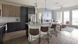 Een moderne keuken met donkere kastjes, een centraal eiland met barstoelen en een zithoek met een bank en tafel.