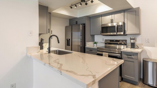 A modern kitchen with a central island, stainless steel appliances, and a grey cabinetry layout. - Landing | Spectacular 1BD, Courtyard (Paradise)