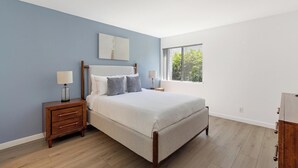 A bedroom with a bed, nightstands, a window with a view, and a wooden floor. - Landing | Spectacular 1BD, Courtyard (Paradise)