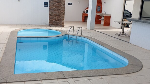A swimming pool with a tiled deck, a brick wall, and a small outdoor seating area. - 2- 3-bedroom apartment with sea view, 100 meters from Atalaia beach (Aracaju)