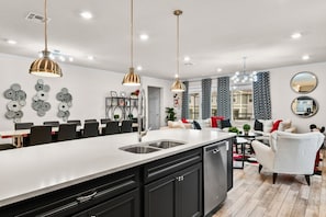 Una cocina moderna con una isla central, iluminación colgante y un comedor con sillas.
