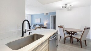 A modern kitchen with a sink, a dining area with a table and chairs, and a living room with a sofa and a lamp. - Landing | Spectacular 2BD, Courtyard (Paradise)