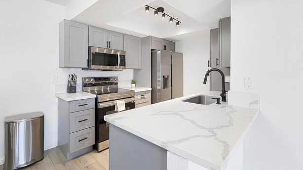 A modern kitchen with grey cabinets, stainless steel appliances, a white marble countertop, and a black faucet. - Landing | Spectacular 2BD, Courtyard (Paradise)