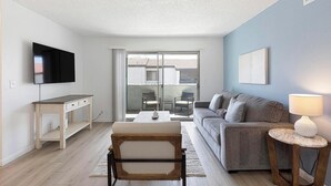 A living room with a sofa, a coffee table, a TV, and a lamp. - Landing | Spectacular 2BD, Courtyard (Paradise)