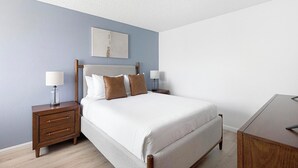A bedroom with a bed, wooden nightstands, a bedside table, and a wall-mounted artwork. - Landing | Spectacular 2BD, Courtyard (Paradise)
