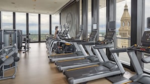 Une salle de sport équipée de tapis de course, d’appareils de musculation et dotée d’une grande fenêtre offrant une vue sur une tour.