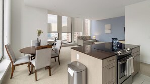 A modern kitchen with a central island, a dining area with chairs, a sofa, and a view of the city through large windows. - Landing | Incredible 2BD, Gym (Hartford)