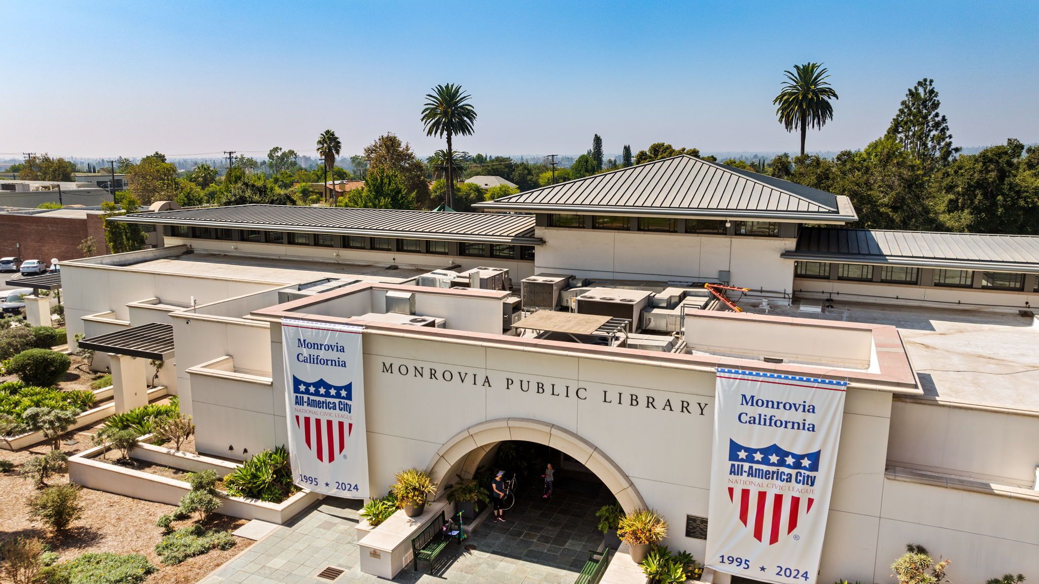 The Monrovia Public Library with a modern architectural design, featuring a prominent entrance and banners indicating its All-America City status.