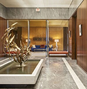 A lobby with a marble floor, a large abstract sculpture, a blue sofa, a wooden bench, and a wall with a textured pattern.