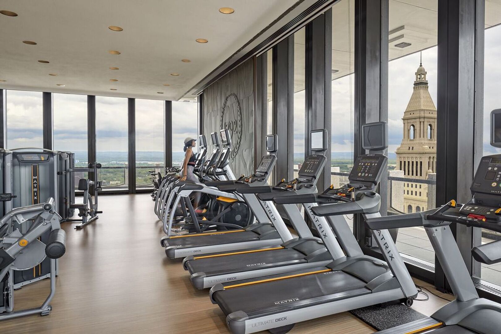 A gym with treadmills, weight machines, and a large window with a view of a tower.