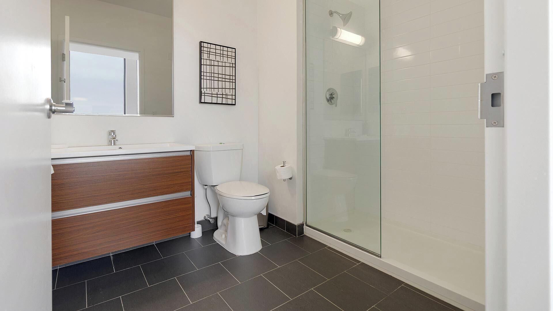 Un baño con inodoro, tocador de madera, cabina de ducha de vidrio y espejo.