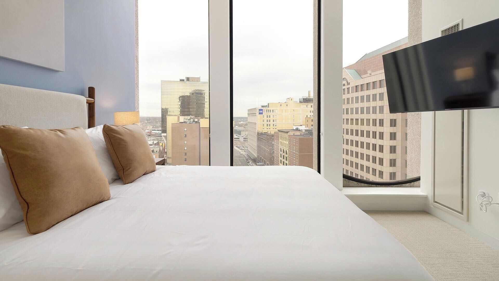 Een hotelkamer met een groot bed, een televisie op een kastje en uitzicht op de stad.