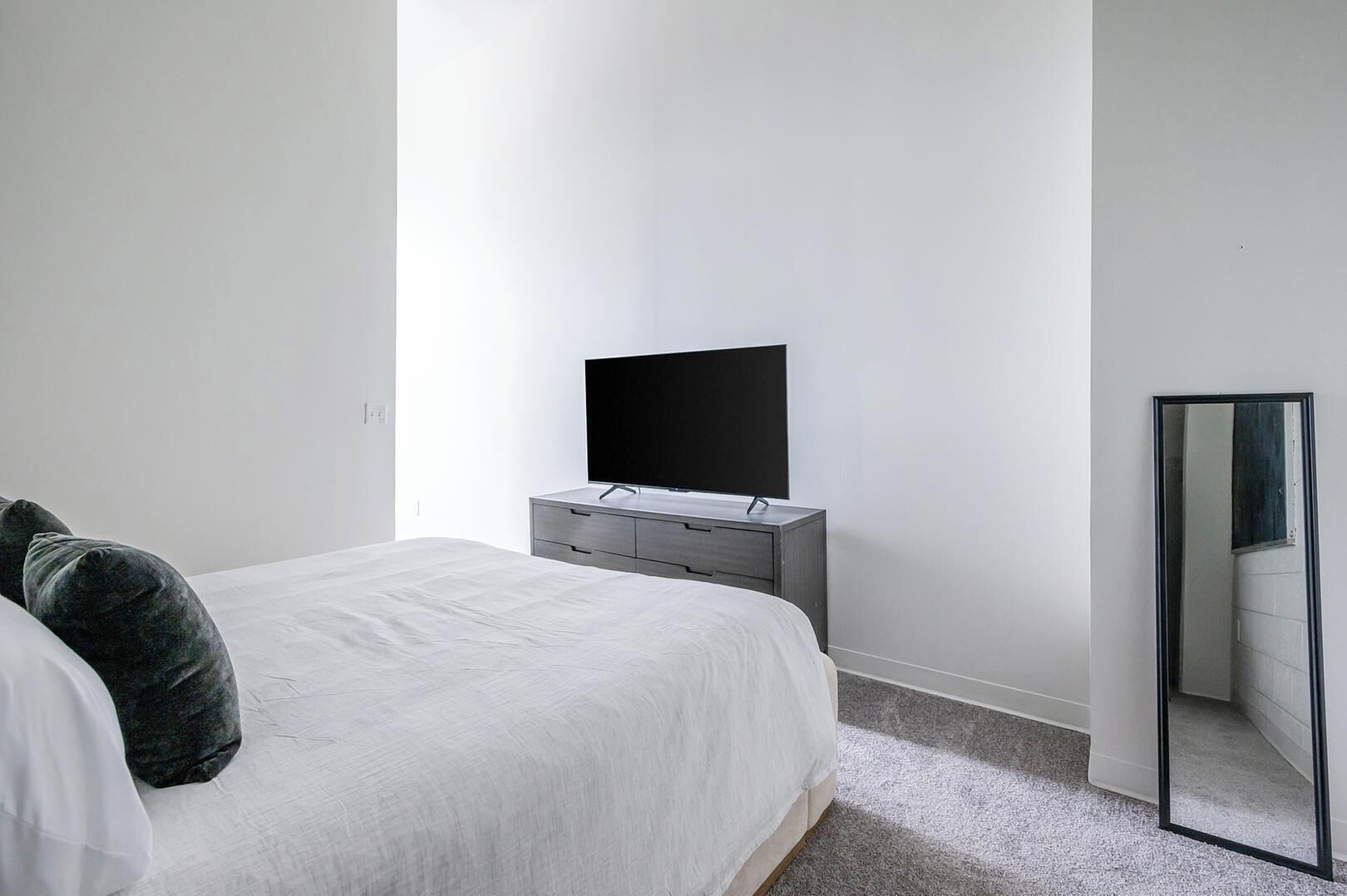 Un dormitori amb un llit, una petita taula de nit, un televisor de pantalla plana i un mirall.