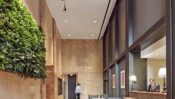 Una hall d'albergo con reception, zona relax e parete verde.
