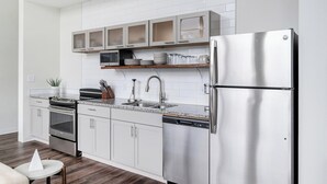 A modern kitchen with white cabinetry, a stainless steel refrigerator, a microwave, and a dishwasher. - Landing | Stylish 1BD, Courtyard (Kansas City)