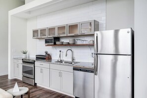 A modern kitchen with white cabinetry, a stainless steel refrigerator, a microwave, and a dishwasher. - Landing | Stylish 1BD, Courtyard (Kansas City)