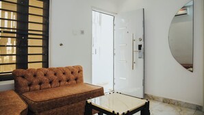 A living room with a brown sofa, a small table, a white door, and a mirror on the wall. - The Rock Aparthotel (Zaria)