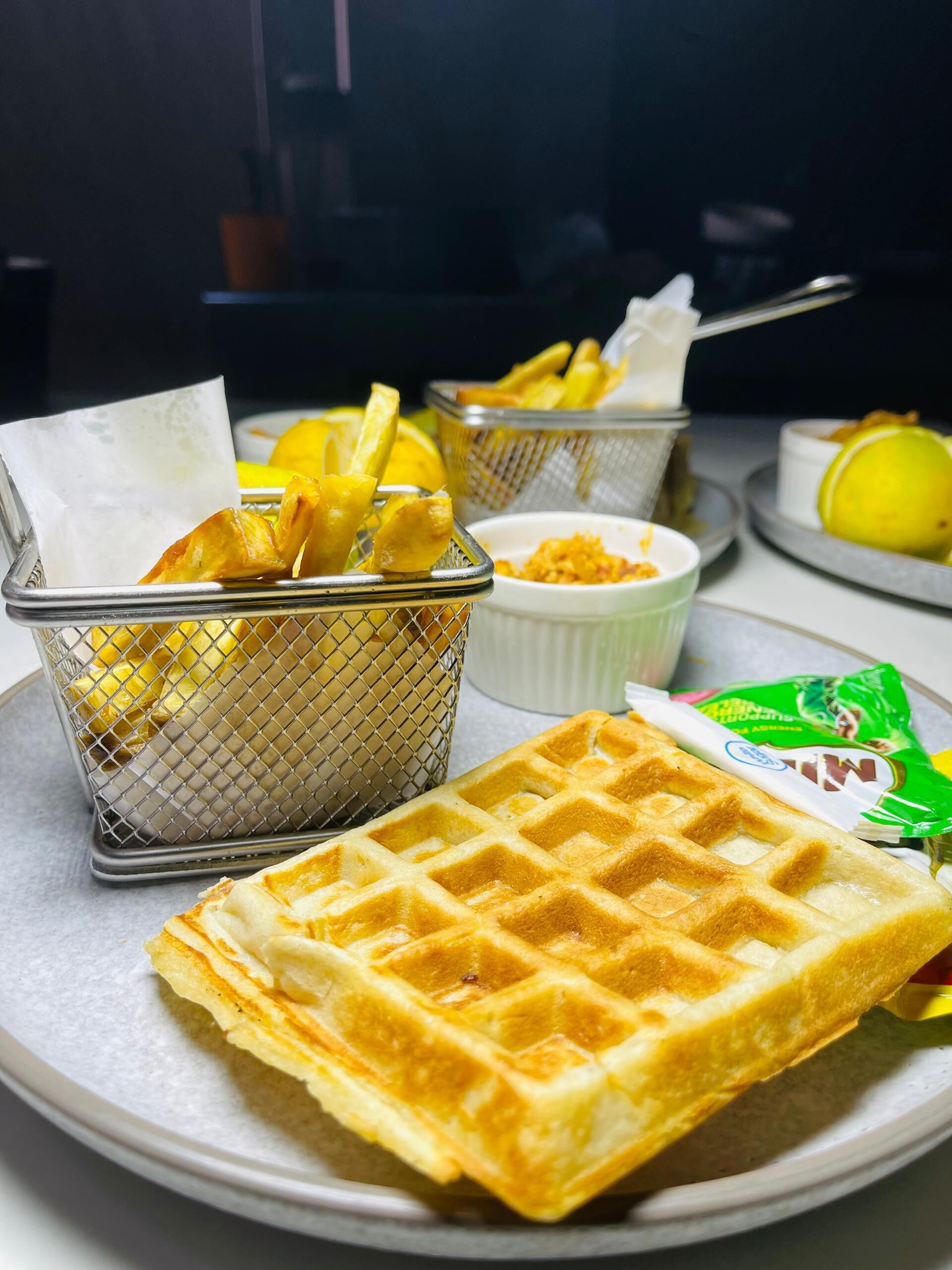 En våffla på en tallrik, tillsammans med en korg med pommes frites och en liten skål med sås.