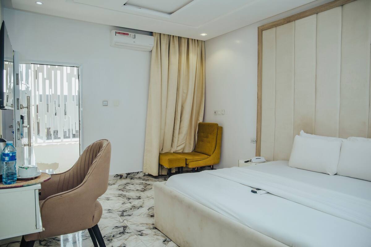Ein Hotelzimmer mit Bett, Schreibtisch, Stuhl, einem Fenster mit Vorhängen und einer Klimaanlage.
