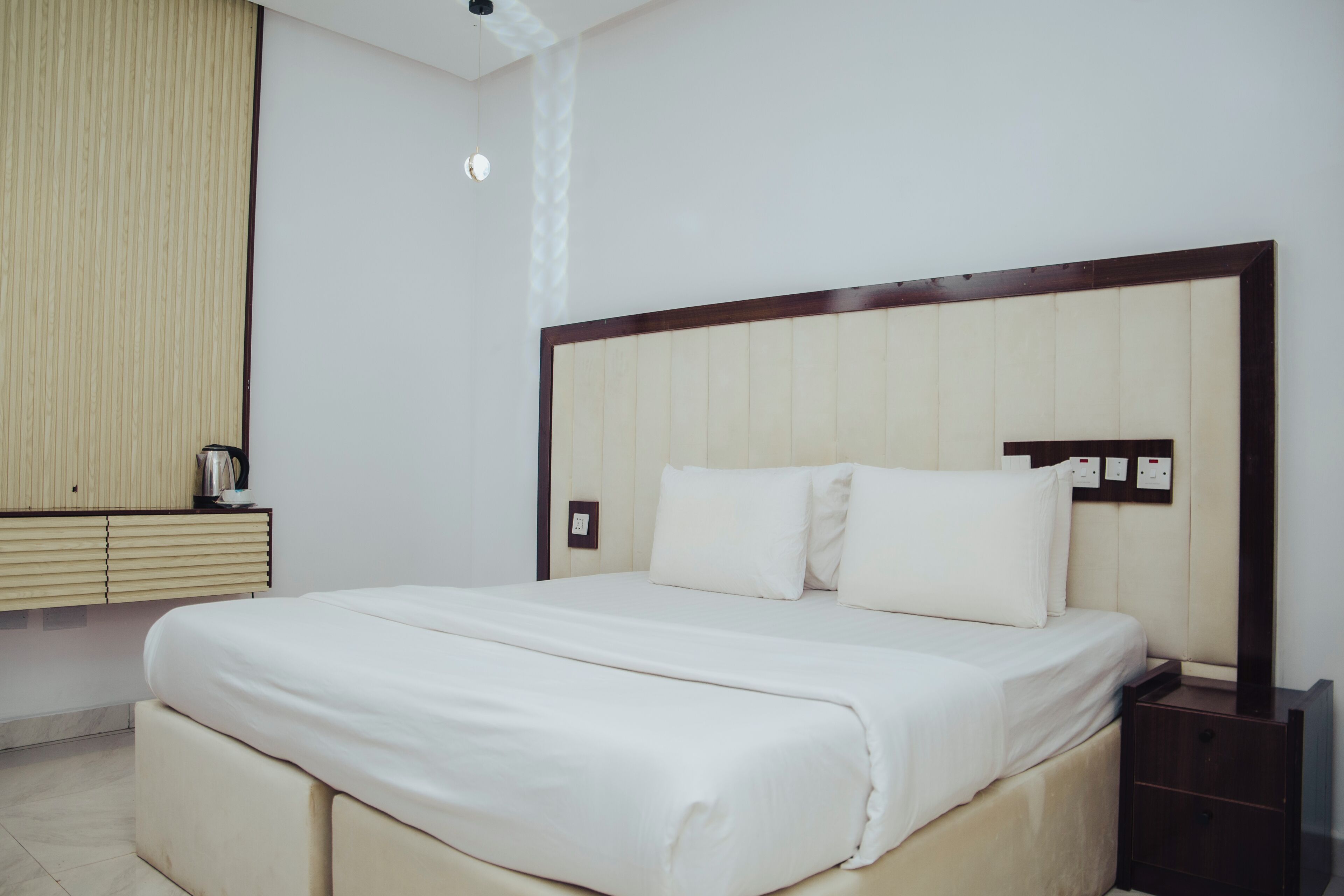 A hotel room with a large bed, a bedside table, a nightstand, and a wall-mounted power outlet.
